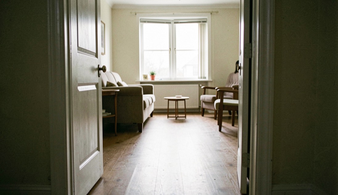 A faceted Venetian mirror with an engraved border hung at eye level on a plain plaster wall opposite a tall window, late morning daylight raking across the facets while the centre plate reflects a quiet corner of the room.